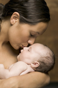 relationship portrait of a young adult mother as she holds and kisses her newborn baby